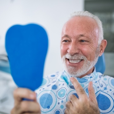 Man in dental chair checking smile in mirror