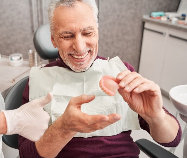 Man in dental chair holding a full denture