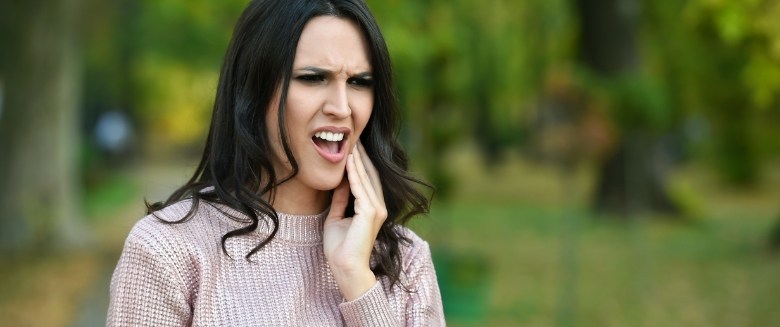 Woman in sweater rubbing her jaw in pain