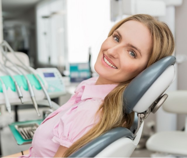 Woman in pink shirt sitting in dental chair and smiling