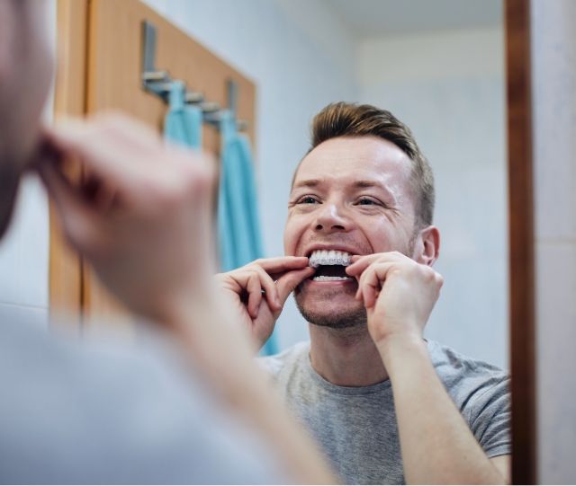 Man in mirror putting on whitening tray